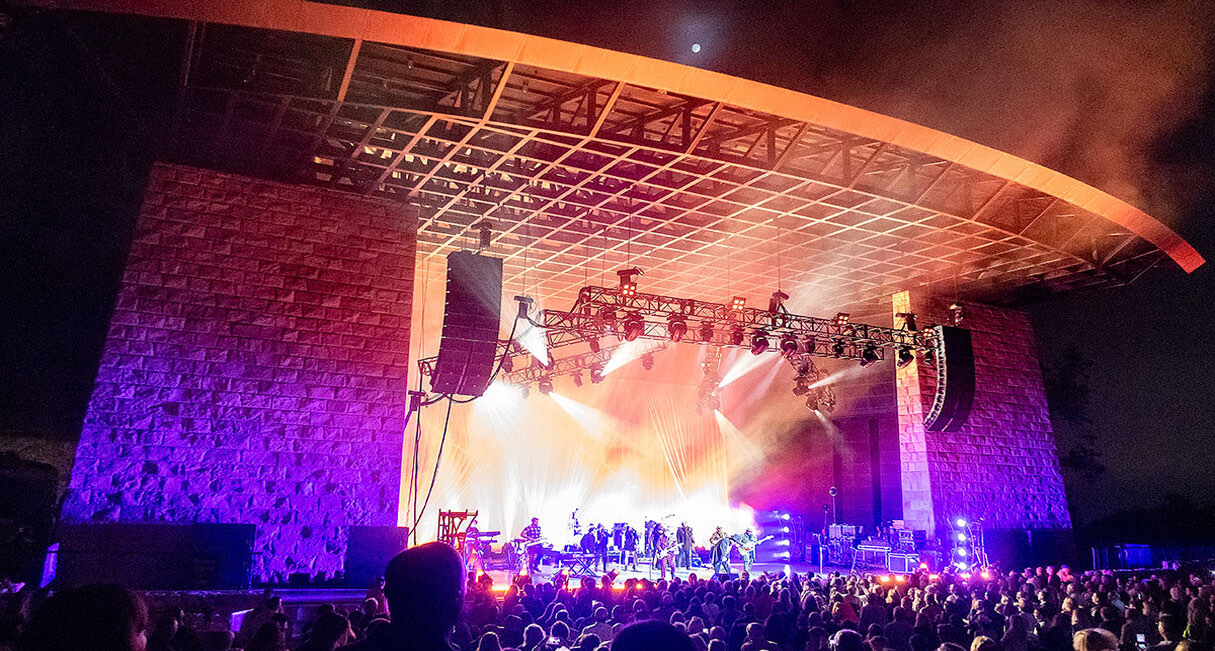The Santa Barbara Bowl amphitheatre lit for a night performance, showing the rebuilt stage canopy and stone walls.
