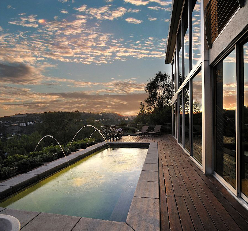 Hollywood Hills Contemporary: a lap pool with arcing fountains beside a glass house, at dusk